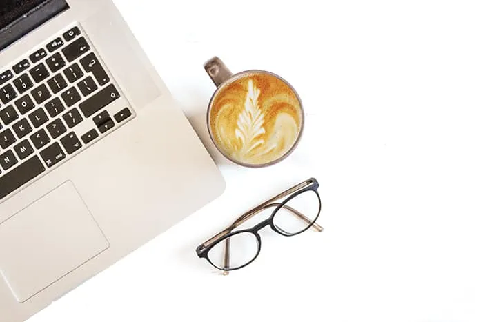 Bureau met cappuccino, opgevouwen computerbril en MacBook
