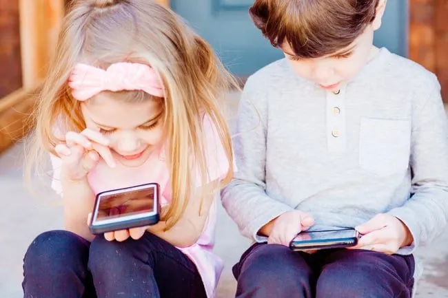 Een meisje en jongetje zittend en bezig op mobieltjes. Het meisje lacht en de jongen is geconcentreerd.