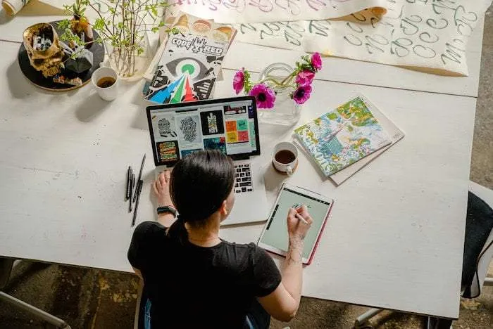 Een vrouw van bovenaf met een laptop en tekentablet in gebruik