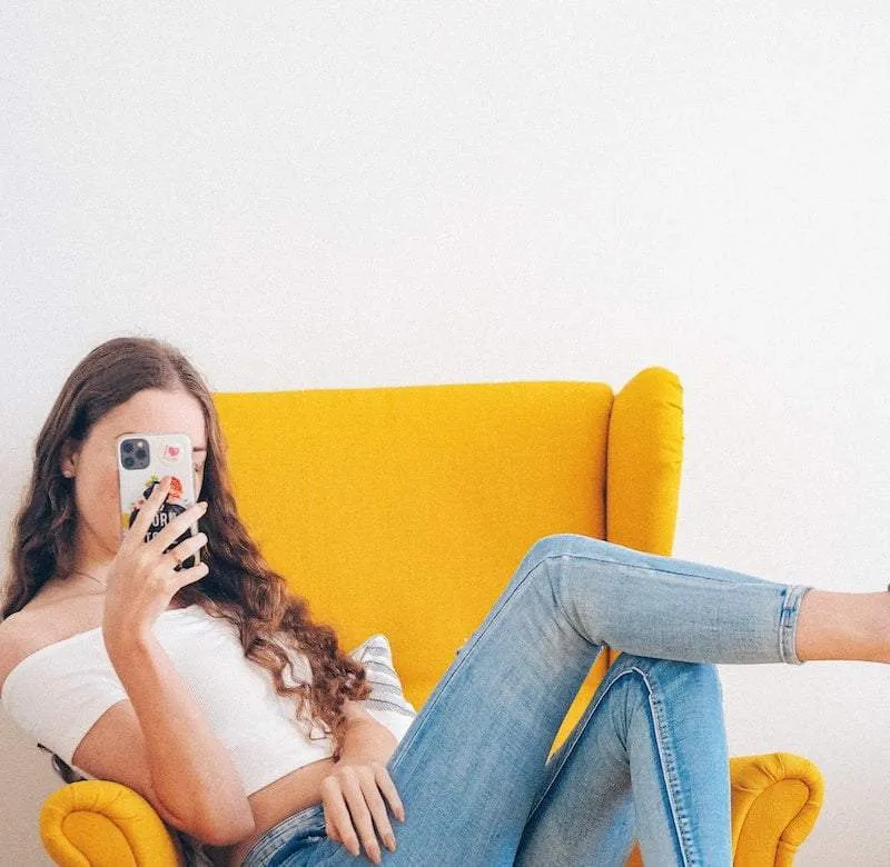 Meisje die op stoel ligt met mobiel voor haar gezicht