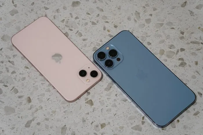 Twee iPhone 13 telefoons naast elkaar op een gevlekte ondergrond en met de de bovenkanten naar elkaar toe