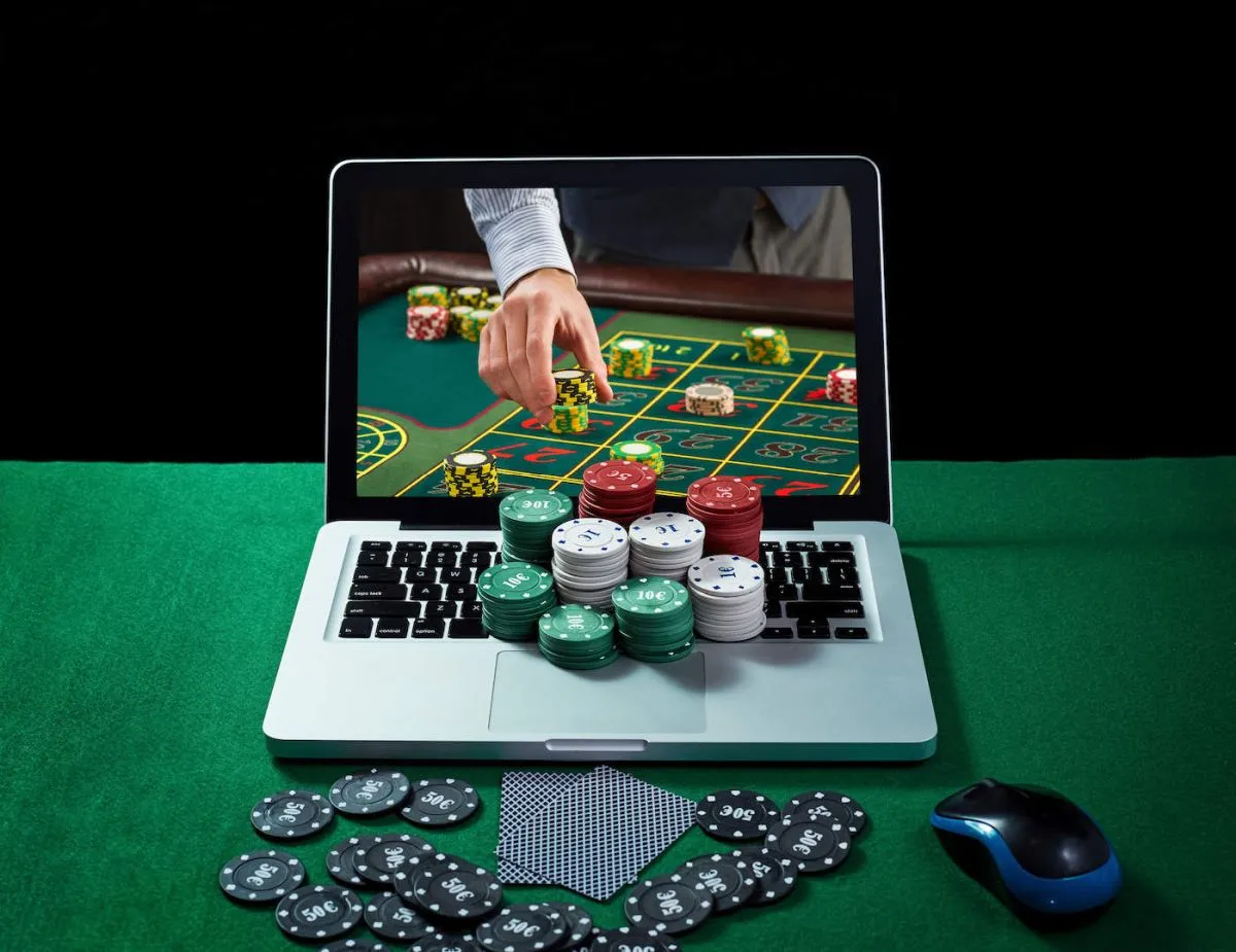 laptop met muntjes op het toetsenbord en kaarten ervoor met op het scherm de hand van een dealer